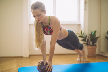 woman doing medicine ball ab exercises at home on a blue yoga mat