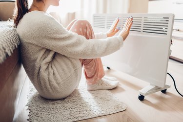 Woman warming her hands by a heater because her hands are always cold