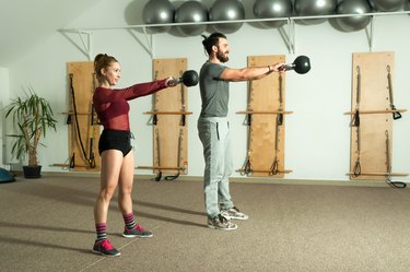 Two athletes performing kettlebell swings at the gym.