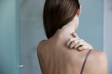 Back view of a person with long brown hair scratching their neck because they have psoriasis