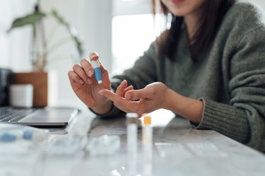 Close up of person wearing a grey sweater and pricking their finger for a blood glucose test, on the counter in their kitchen