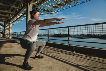 Woman doing iso squat holds with a resistance band on a pier