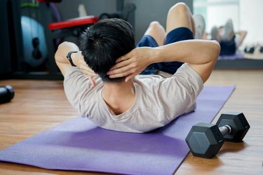 rear view of person doing single-dumbbell ab workout on purple yoga mat with weight