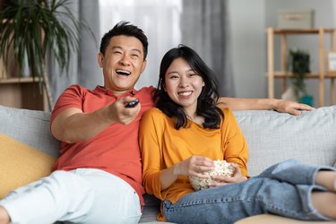 a couple sitting on the couch eating popcorn and watching a funny movie, as a nighttime habit to reduce inflammation