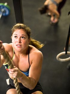 Female athlete performing rope climbing in CrossFit gym