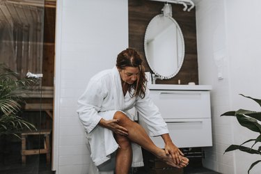 a person in a bathrobe applying lotion to their itchy legs