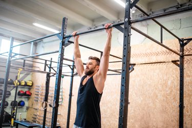 Person wearing black tank top performing a dead hang in the gym