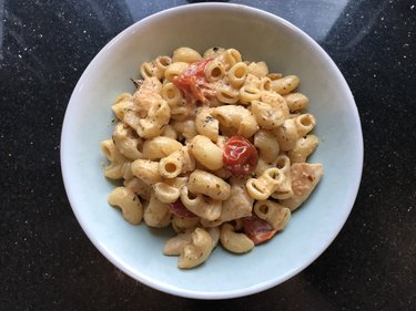 an overhead photo of a white bowl of pasta made with Boursin cheese, chicken and tomatoes