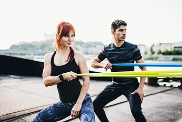 Fit man and woman exercising with resistance bands outdoors