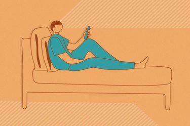 Person wearing blue outfit lounging in bed scrolling on a phone