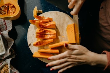 close view of a person slicing a butternut squash on a wooden cutting board, to represent foods that cause carotenemia