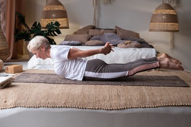 Older adult doing locust pose on yoga mat in bedroom
