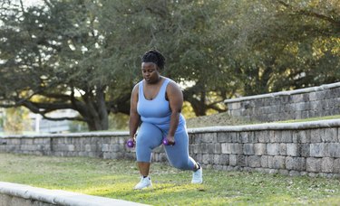 Person wearing blue tank top and leggings doing a Tabata workout outdoors in park.