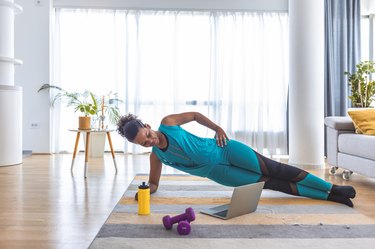 woman doing a side plank exercise with purple dumbbells in her living room