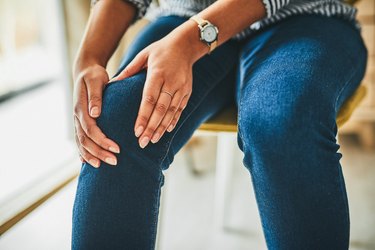 close view of a person wearing jeans and a striped shirt holding their knee because of arthritis in the knees