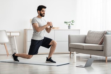 Person in gray T-shirt and black shorts performing a lunge in their living room as part of a beginner HIIT workout.