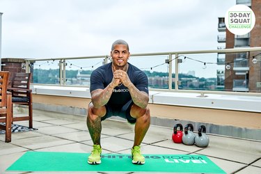 Fhitting Room trainer demonstrating squat form on a rooftop with green mat during 30-day squat challenge