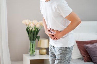 Person standing in a bedroom holding their abdomen visibly in pain