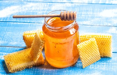 Glass jar of honey on blue wooden table with honeycomb nearby to illustrate what local honey is and local honey benefits