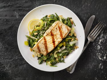 overhead photo of halibut with spinach, leeks and pine nuts to improve brain health on gray table with fork and knife