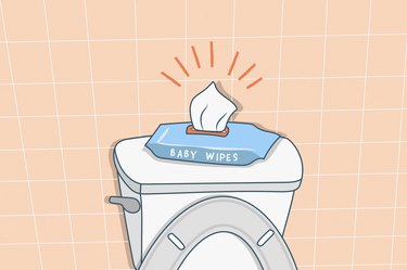 An illustration of a package of open baby wipes on the back of a toilet , in a bathroom with peach tile