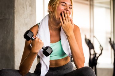 Woman lifting a dumbbell and yawning during her workout
