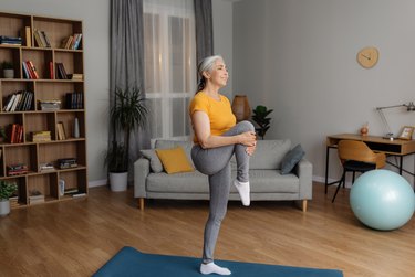 Older adult balancing on one leg as part of a standing Pilates workout.