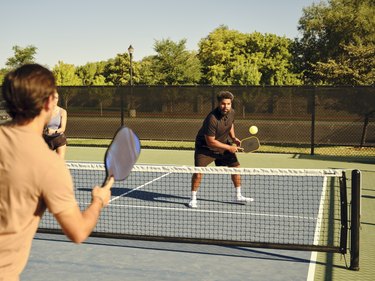 Two people playing pickleball on a court in the summer.