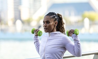 Person in workout clothes lifting weights outdoors to demonstrate a dumbbell shoulder workout.