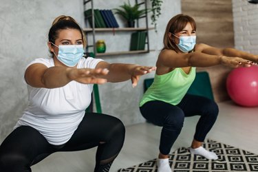 Friends wearing a mask while exercising together at home doing jump squats