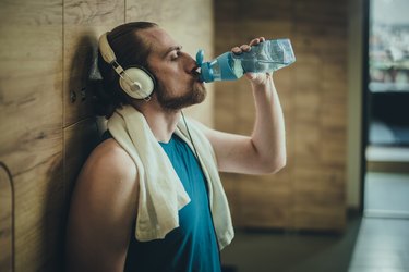 man wearing headphones and drinking a bottle of water during workout