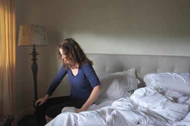 woman sitting on her bed and feeling confused or disoriented after waking up