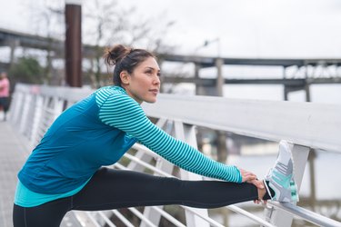 Person in blue jacket and black leggings stretching outside after a run.
