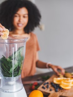 Woman placing fruit into blender with spinach for smoothie