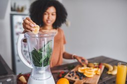 Woman placing fruit into blender with spinach for smoothie