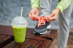 Sports nutrition smoothie next to person tying shoes before workout