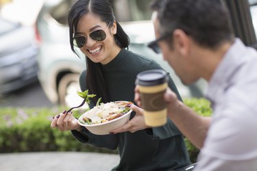 a person with long black hair smiling and wearing sunglasses outside while eating a salad to protect their eye health