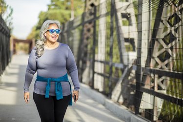 Older adult in gray long-sleeve shirt and black leggings walking outside to demonstrate LISS cardio