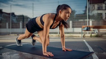 Beautiful Energetic Fitness Girl Doing Mountain Climber Exercises. She is Doing a Workout in a Fenced Outdoor Basketball Court. Evening After Rain in a Residential Neighborhood Area.