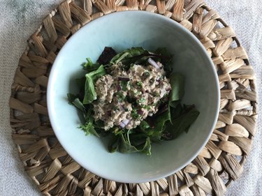 an overhead photo of a 10-minute sardine salad on a bed of greens in a bowl on a wicker placemat on a white marble counter