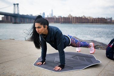 athlete wearing a black hoodie and doing a plank outdoors with muscles shaking